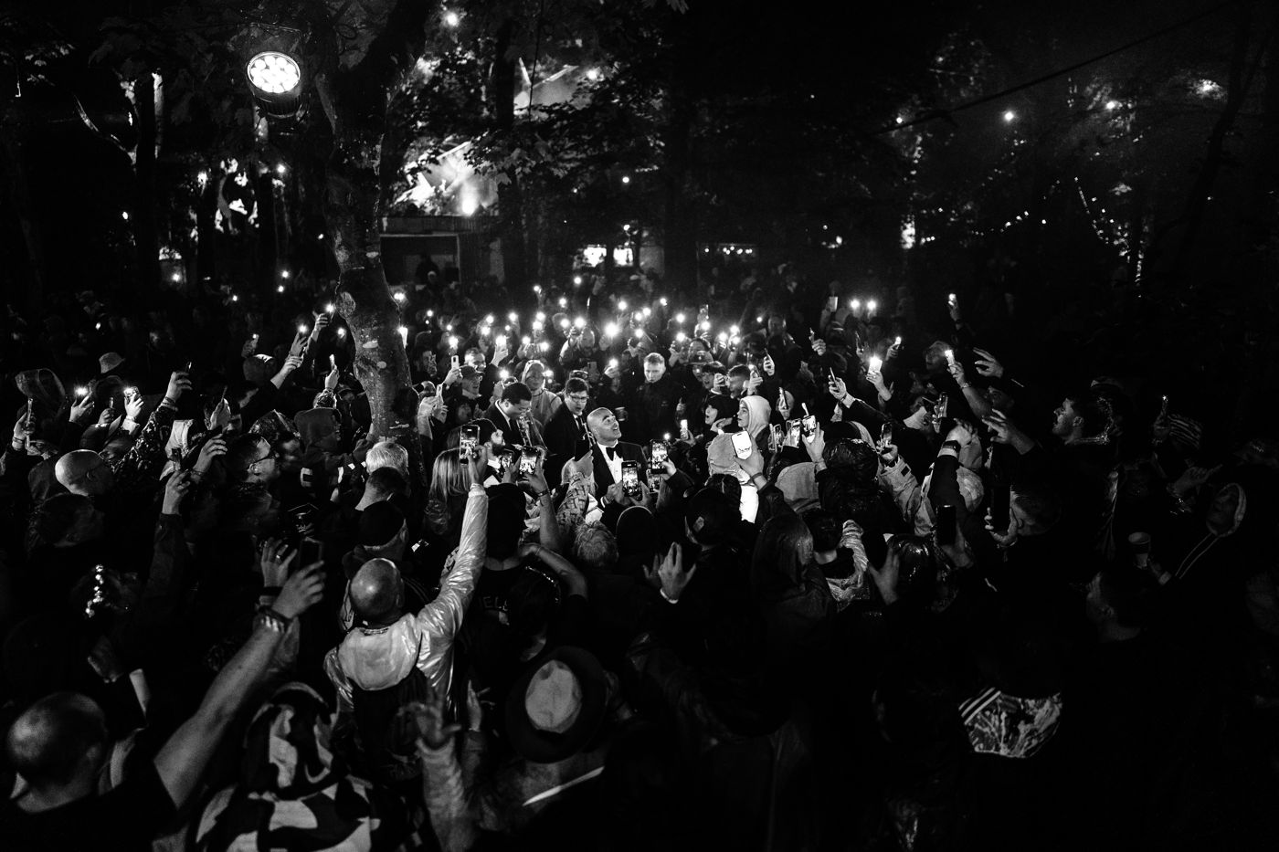 Black and white photo of Luke and the horn section surrounded by a festival crowd at night, hundreds of phone lights raised